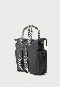 Bolsa tote negra con bolsillos laterales, herrajes dorados y correas y asas de mano desmontables con estampado de cebra sobre un fondo blanco.