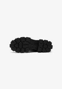 Semelle de chaussure en caoutchouc noir avec un motif de semelle présentant de profonds rainures et des crampons arrondis pour une meilleure traction et adhérence. Design à surface plate.