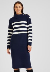 Abito lavorato a maglia blu navy con strisce orizzontali bianche, colletto alto e tre bottoni decorativi sulla spalla. Texture morbida e lunghezza media.