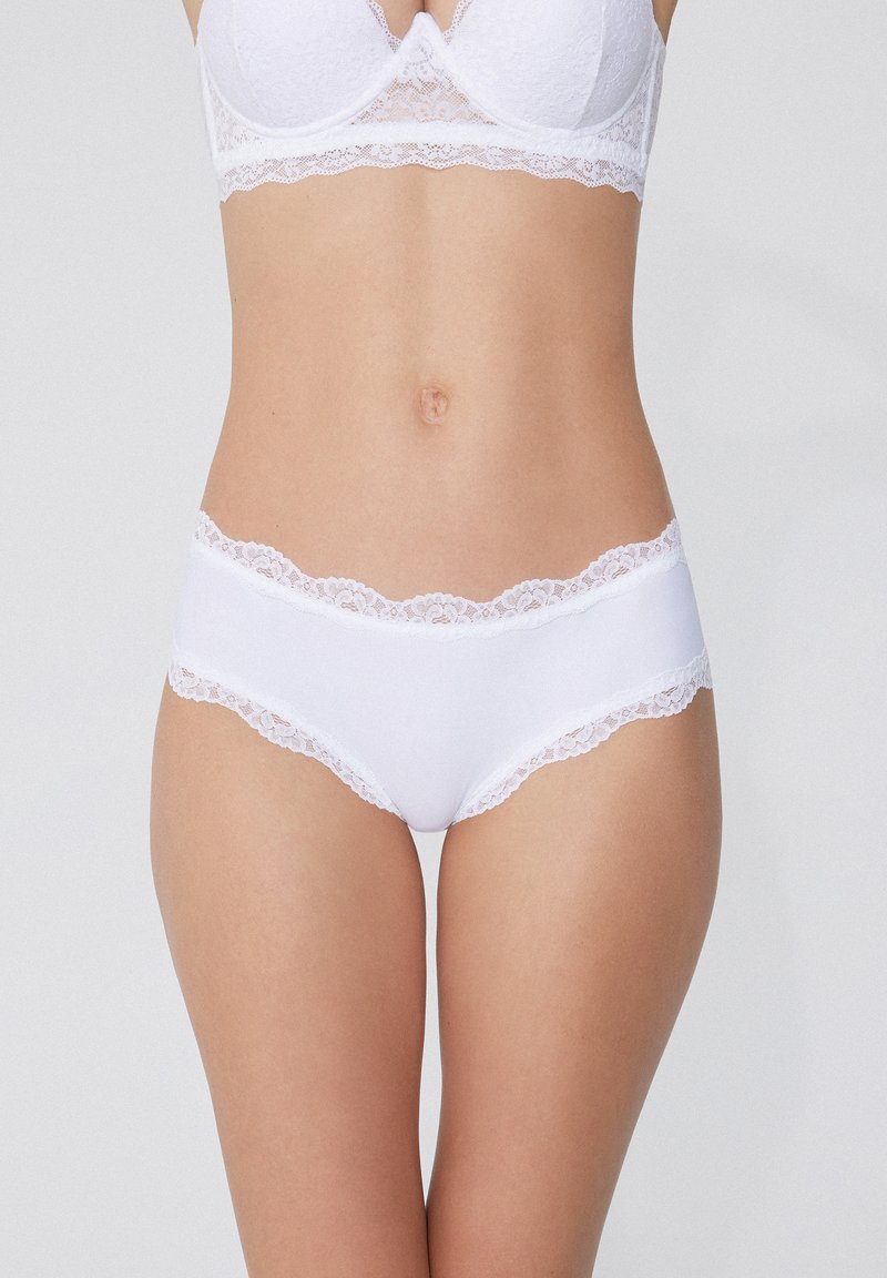 Białe majtki z koronkowym wykończeniem, wykonane z miękkiego materiału o gładkiej teksturze, z kwiecistymi akcentami koronki wzdłuż talii i otworów na nogi.
