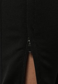 Black denim fabric with a close-up view of a zipper detail on the side. The zipper is closed, revealing a smooth texture and clean lines.