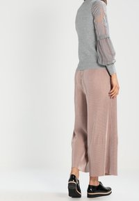 Szary dzianinowy sweter z przezroczystymi, haftowanymi puff sleeves; w parze z jasnoróżowymi spodniami w szerokim kroju z plisami; czarne buty z grubą podeszwą.