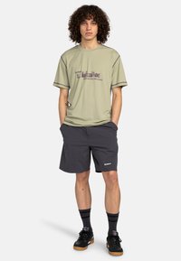 Light green short-sleeve shirt with text design, paired with dark gray shorts. Black sneakers and striped socks complete the outfit.