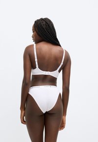 Hvidt bomulds-bh- og g-strengsæt med stropper med logo. Bhen har justerbare stropper og lukning med hægte bagpå.