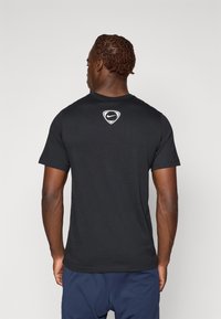 T-shirt noir à manches courtes en coton, avec un col rond et un logo Nike blanc en forme de blason sur le haut du dos.
