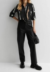 Czarna bluzka z abstrakcyjnymi beżowymi i białymi wzorami, zestawiona z czarnymi skórzanymi spodniami z wysokim stanem i masywnymi czarnymi botkami.