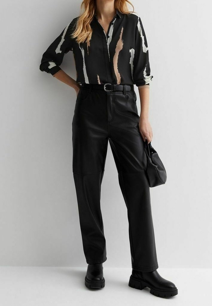 Czarna bluzka z abstrakcyjnymi beżowymi i białymi wzorami, zestawiona z czarnymi skórzanymi spodniami z wysokim stanem i masywnymi czarnymi botkami.
