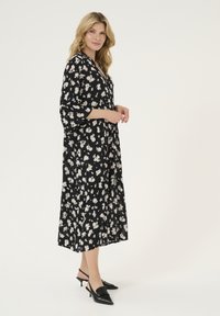 Černé květinové maxi šaty s tříčtvrtečními rukávy, A-linie, s bílým vzorem květin, doplněné černými špičatými slingback podpatky.