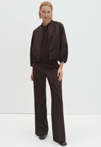 Bruine bomberjack met rits, geribbelde manchetten, gedragen over een donker gebreide top, gecombineerd met wijde broekspijpen, ook in bruin. Gladde stoftextuur.