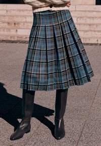 Niebieska midi spódnica w kratę z plisami i detalem w pasie, zestawiona z wysokimi brązowymi skórzanymi kozakami. Teksturowana tkanina z kontrastującymi brązowymi akcentami.