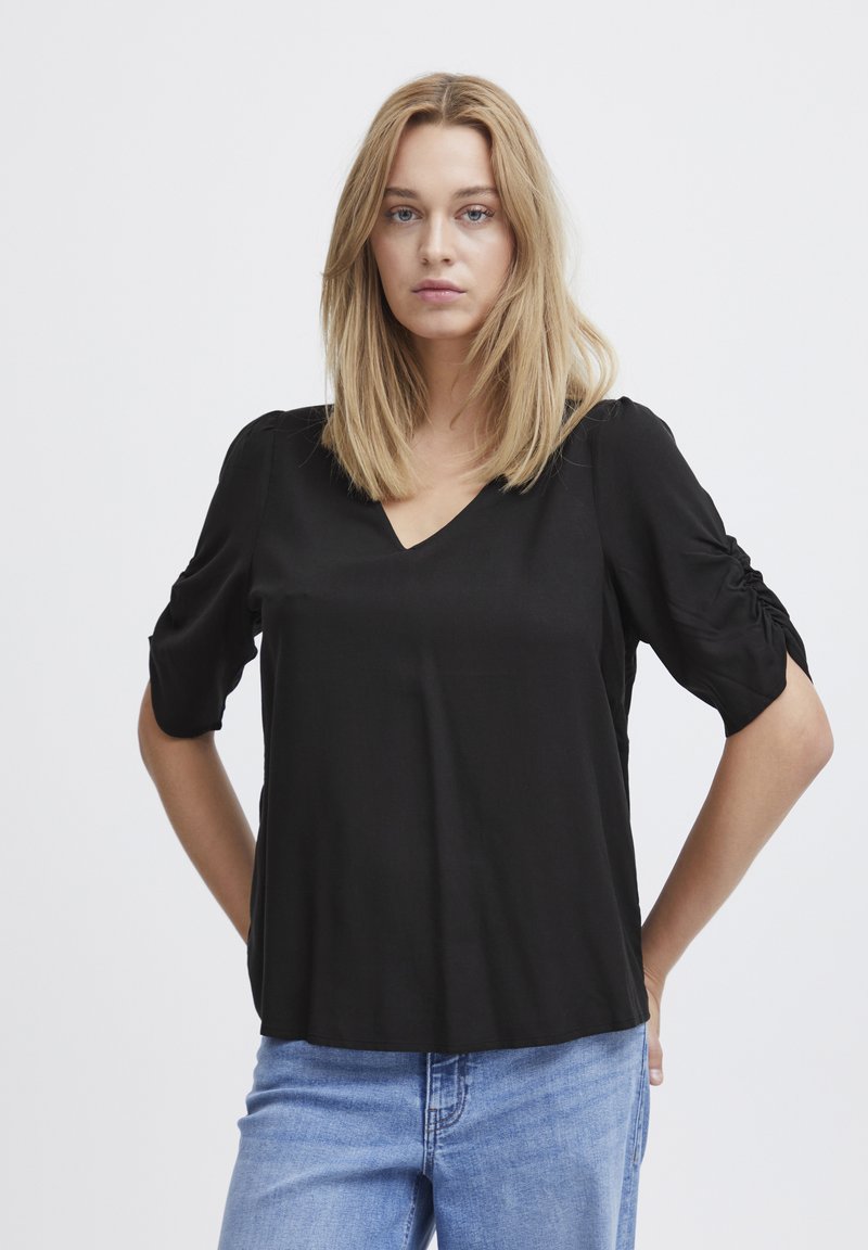 Maglietta nera a maniche corte con scollatura a V in tessuto leggero; presenta dettagli arricciati sulle maniche; abbinata a jeans in denim blu.