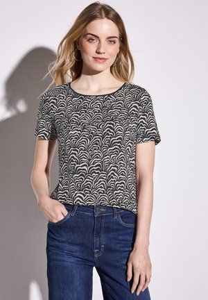 Maglietta a maniche corte nera con motivo ondulato bianco sporco, scollatura tonda e vestibilità rilassata, abbinata a jeans blu scuro.