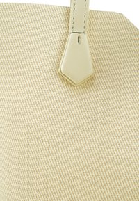 Beige textuur tote bag met een gladde, crème-kleurige leren handgreep met een geometrische accent in de bovenhoek.