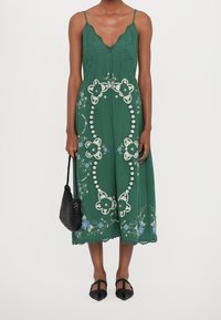 Zelené midi šaty s tenkými ramínky, květinovou výšivkou, krajkovým lemem a volným střihem. V kombinaci s černou tkanou taškou a plochými botami.