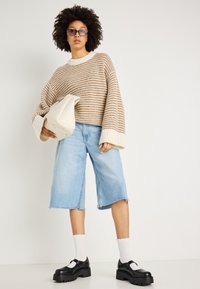 Neulepaita, jossa on vaaleanbeigejä ja ruskeita raitoja, lyhyt malli, leveät hihat; vaaleansiniset farkkuhousut; mustat platform-kengät; vaaleankermanvärinen laukku.