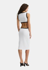 Set due pezzi a coste bianche, composto da un top cropped con bordo nero e una gonna midi aderente. Indossato con sandali neri con tacco blocco.