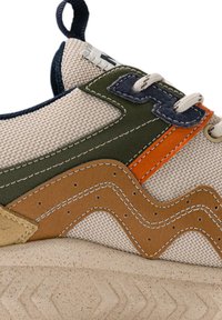 Sneaker met een beige mesh bovenwerk met groene, oranje en bruine leren accenten, een getextureerd golfpatroon en een rubberen zool met een zigzagprofiel.