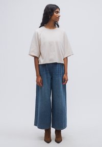 Φωτεινό μπεζ cropped φούτερ σε συνδυασμό με φαρδιά μπλε τζιν παντελόνια. Το φούτερ έχει στρογγυλό λαιμόκοψη και κοντά μανίκια.