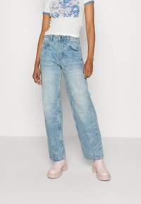 Jeans azul claro com um padrão marmoreado, corte solto e cintura alta. Combinados com uma t-shirt branca com detalhes azuis e sapatilhas de plataforma rosa claro.