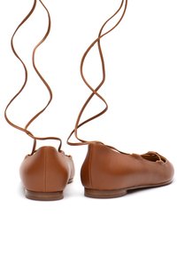 Ballerine in pelle marrone con una superficie liscia, dotate di legature incrociate alla caviglia e punta rotonda, posizionate su uno sfondo bianco.