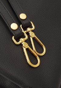 Sort lædertaske med guldfarvet hardware, der har dobbelt snapknapper og to klaplåse til sikker vedhæftning. Tekstureret overflade.