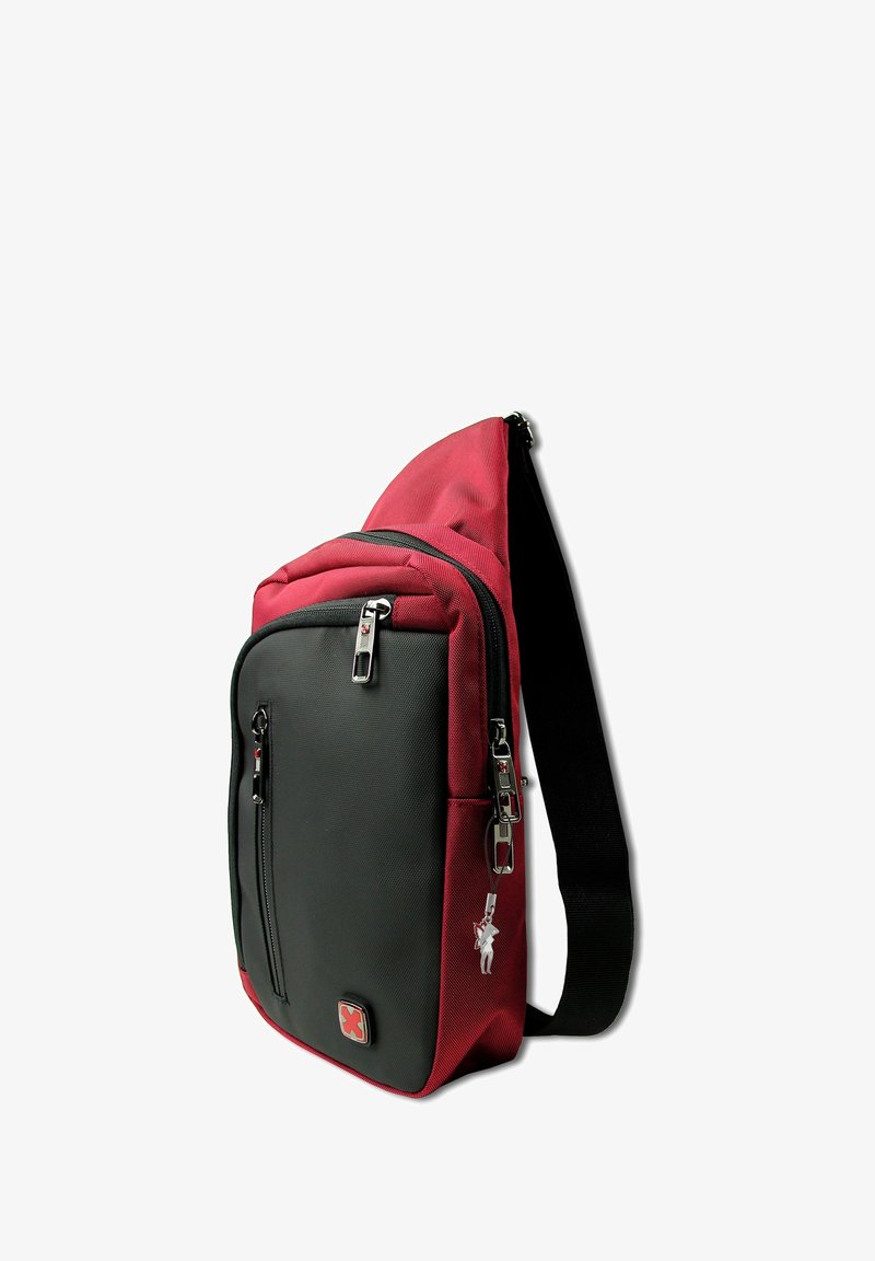 Sac à bandoulière rouge et noir avec plusieurs compartiments zippés et une sangle noire ajustable, se tenant debout sur un fond blanc.