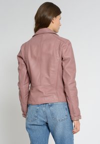 Veste en cuir rose au design ajusté, avec des détails de couture visibles et des accents en métal argenté. Associée à un jean bleu taille haute.
