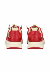 Un paio di sneakers rosse e beige mostrate da dietro, con una suola bianca spessa e passanti per lacci marroni su uno sfondo bianco.