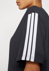 Schwarzes T-Shirt mit kurzen Ärmeln, versehen mit drei weißen Streifen auf der Schulter. Aus Baumwolle, mit glatter Textur und lässiger Passform.