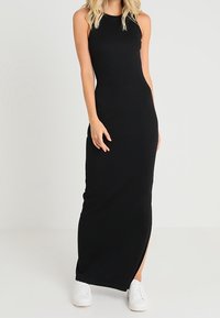 Musta, hihaton ribbattu maksimekko, jossa on sivureikä. Tiukka malli, pehmeä rakenne, yhdistettynä valkoisiin tennareihin.