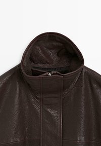Burgundy läderjacka med hög krage, slät textur och framzip; matt yta med subtila ådringsdetaljer.