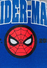 Il tessuto in maglia blu presenta un grande cerchio nero con un design della maschera di Spider-Man rossa al centro, occhi bianchi e accenti di un motivo a ragnatela nera.