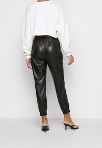 Vit kortärmad sweatshirt med långa ärmar, i kombination med blanka svarta byxor med elastiskt midjeband och svarta klacksandaler, sedd bakifrån.