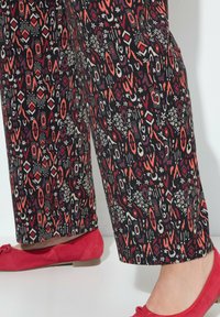 Tiskované kalhoty s černým pozadím a barevnými geometrickými a květinovými vzory; v kombinaci s červenými plochými botami.