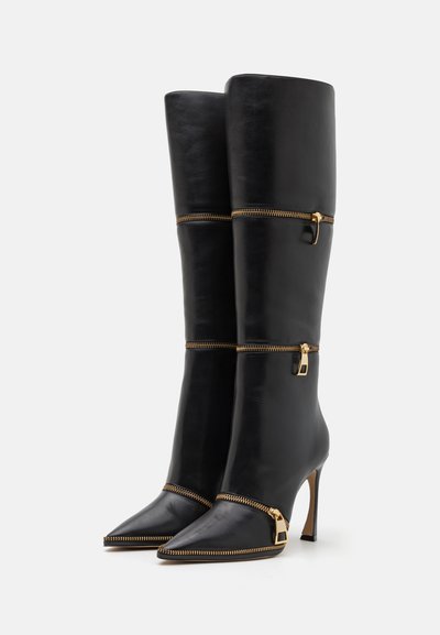 Knielange zwarte leren laarzen met puntige neuzen en gouden ritsaccenten, met een elegante uitstraling en een hoge stilettorahakken.