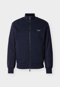 Ναυτικό bomber μπουφάν με ψηλό γιακά, υφασμάτινο σώμα και αντίθετες λείες μανίκια. Διαθέτει φερμουάρ κλεισίματος και μικρή λεπτομέρεια με λογότυπο με φτερά.