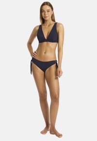 Zestaw bikini w kolorze granatowym składający się z trójkątnego topu oraz dołu z wiązaniem po bokach. Materiał jest gładki, z minimalnymi elementami metalowymi i prostym designem.