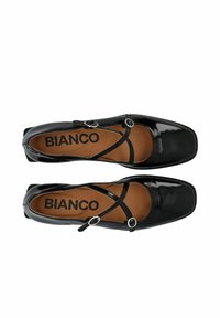 Zapatos de charol negro con punta cuadrada, tiras cruzadas y herrajes de color plateado. La plantilla presenta el logo "BIANCO."