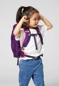 Lila Kinder-Rucksack mit pinkem Schuppenmuster, verstellbaren Trägern und Schnallen. Getragen von einem Kind in einem weißen Shirt und Jeans.