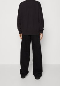 Felpa nera oversize con spalle scese, polsini e orlo a costine. Abbinata a pantaloni neri a vestibilità ampia, caratterizzati da una texture liscia.