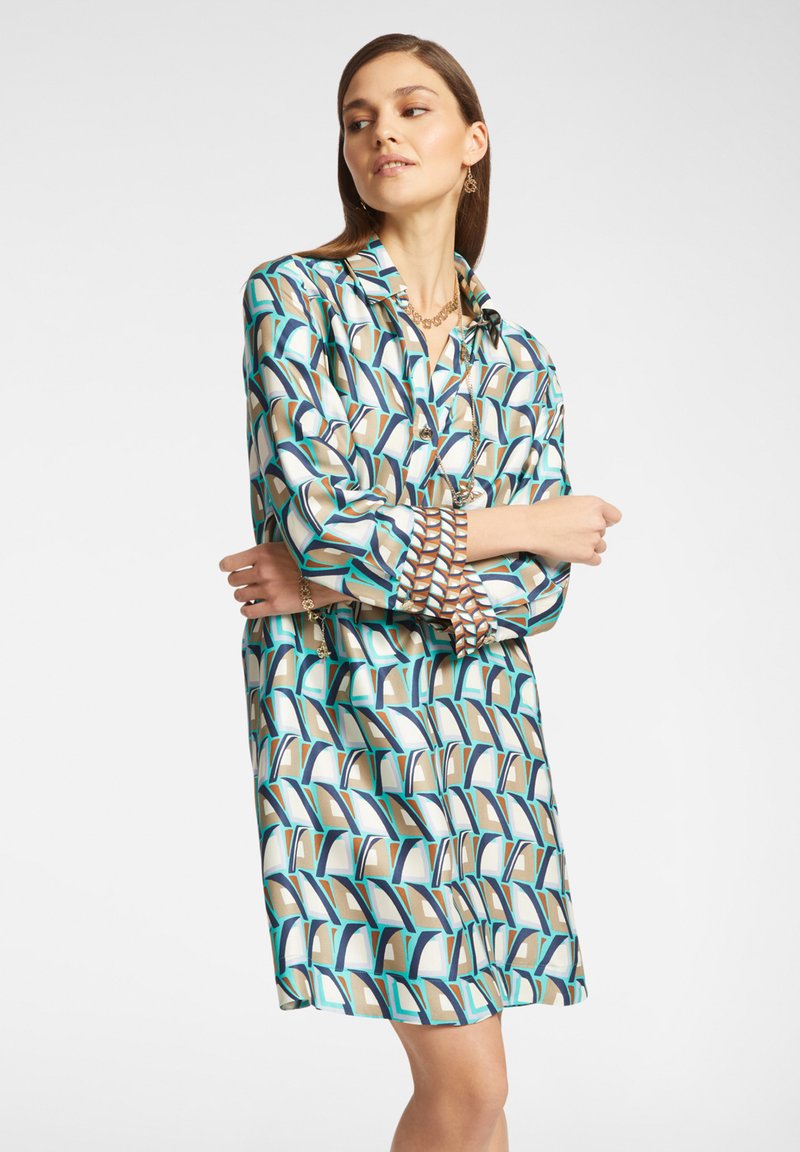Vestito camicia con un motivo geometrico in turchese, marrone e crema. Dotato di colletto e chiusura a bottoni, con maniche lunghe e vestibilità comoda.