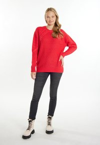 Pulover roșu tricotat cu un model texturat de cabluri, asortat cu blugi negri skinny și cizme de luptă bej cu șireturi.