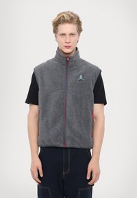 Gray fleece vest with a high collar, red zipper, and side pockets. Features a small logo on the chest and a relaxed fit.