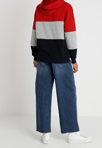 Felpa con cappuccio a blocchi di colore rosso, grigio e blu navy con tasca a marsupio, abbinata a pantaloni in denim a gamba larga e sneakers bianche.