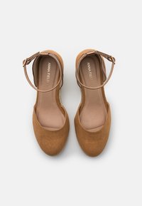 Scarpe flat di suede marrone con cinturino alla caviglia, punta arrotondata e soletta leggermente imbottita. Il nome del marchio "ANNA FIELD" è visibile sulla soletta.