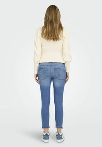 Suéter de canalé ligero con mangas abullonadas, combinado con jeans ajustados de tiro medio en azul, que presentan un dobladillo deshilachado y dos bolsillos traseros.