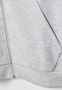 Šedá mikina na zip vyrobená z hladkého, texturovaného materiálu. Disponuje kovovým zipem a šikmými bočními kapsami. Jednoduchý design s minimálním prošíváním.