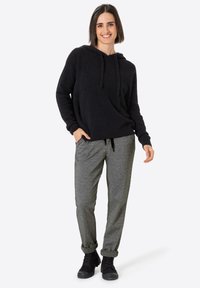 Schwarzer Hoodie mit Kordelzug, lässige Passform. Graue gemusterte Hose mit hochgerollten Bündchen. Schwarze Sneaker vervollständigen das legere Outfit.