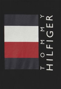 Sort stof med et rektangulært logo med tre vandrette striber: marineblå, hvid og rød, sammen med teksten "TOMMY HILFIGER" i fed hvid.