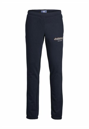Námořnická modrá zipová mikina s kapucí a odpovídajícími tepláky, které mají malé logo na hrudi a po straně. Materiál je měkký a strukturovaný.